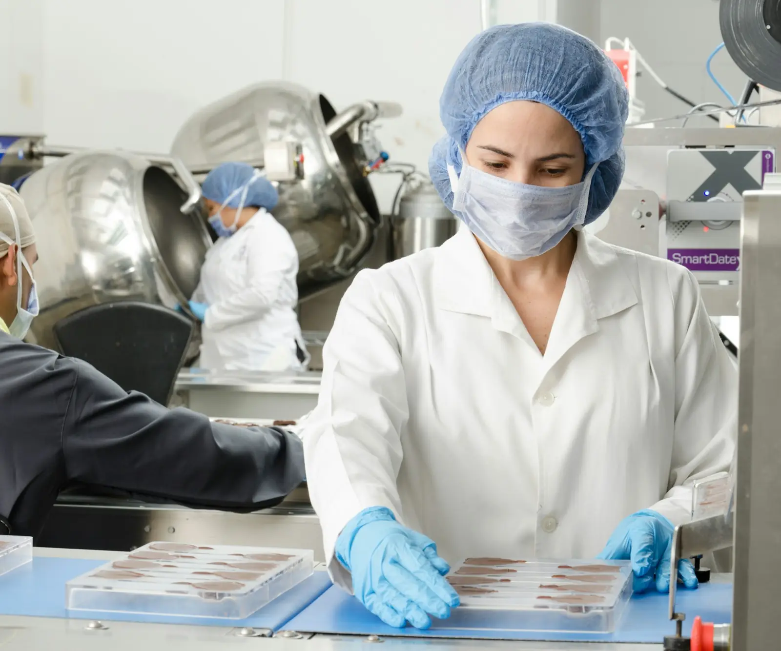 Mitarbeitende mit Haarnetz, Mundschutz und Handschuhen an einer Produktionslinie.